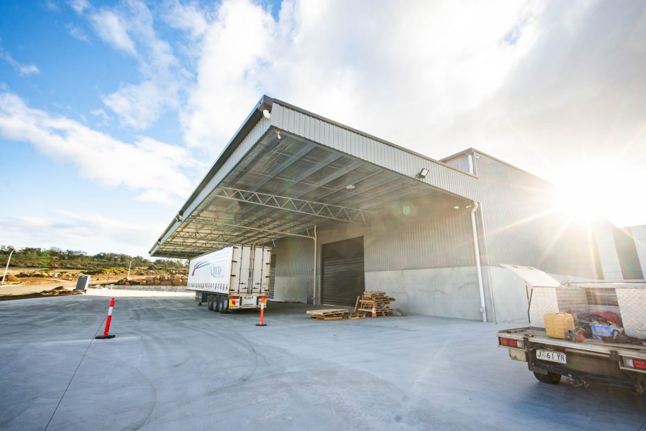 Truck unloading at a warehouse construction site with covered loading bays and reinforced concrete flooring.
